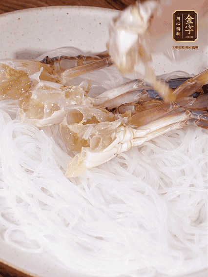 盤底墊上粉絲，擺上梭子蟹、火腿片，撒姜粒，淋上蒸魚豉油、花雕酒調味腌制15分鐘